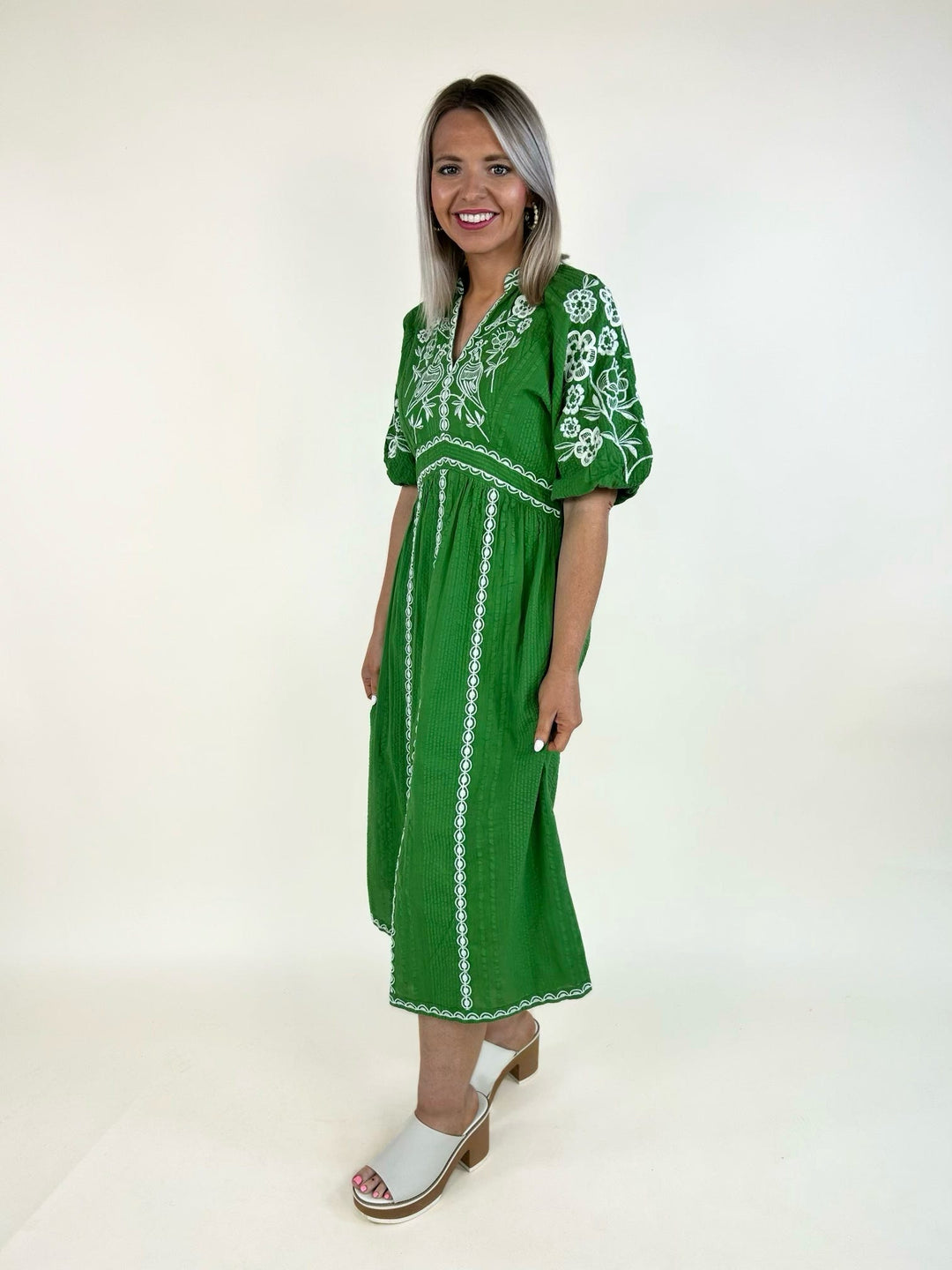 Side view of emerald green embroidered midi dress with puff sleeves, white embroidery, and relaxed fit
