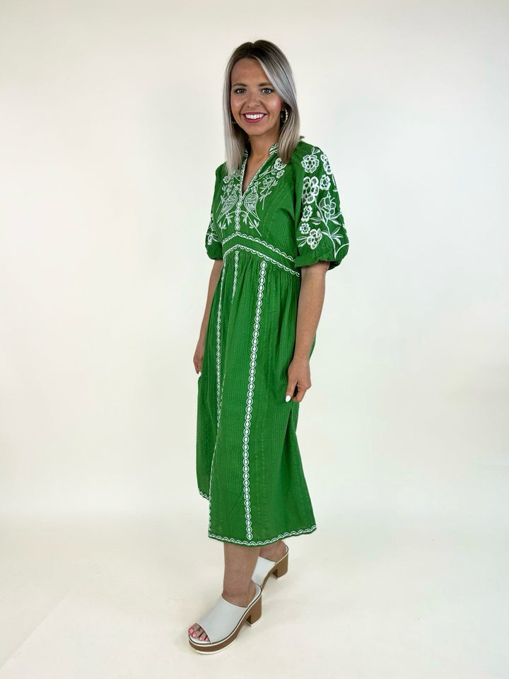 Side view of emerald green embroidered midi dress with puff sleeves, white embroidery, and relaxed fit