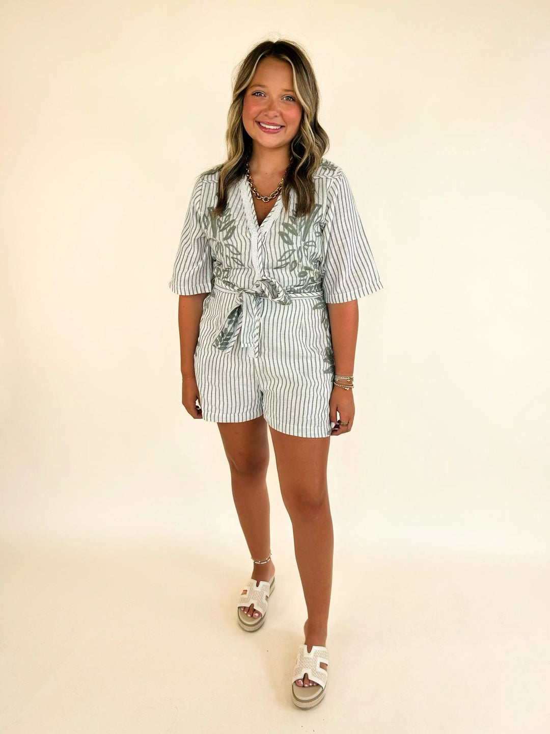 Women's olive embroidered belted romper with botanical embroidery, striped fabric, scalloped trim, and V-neckline.