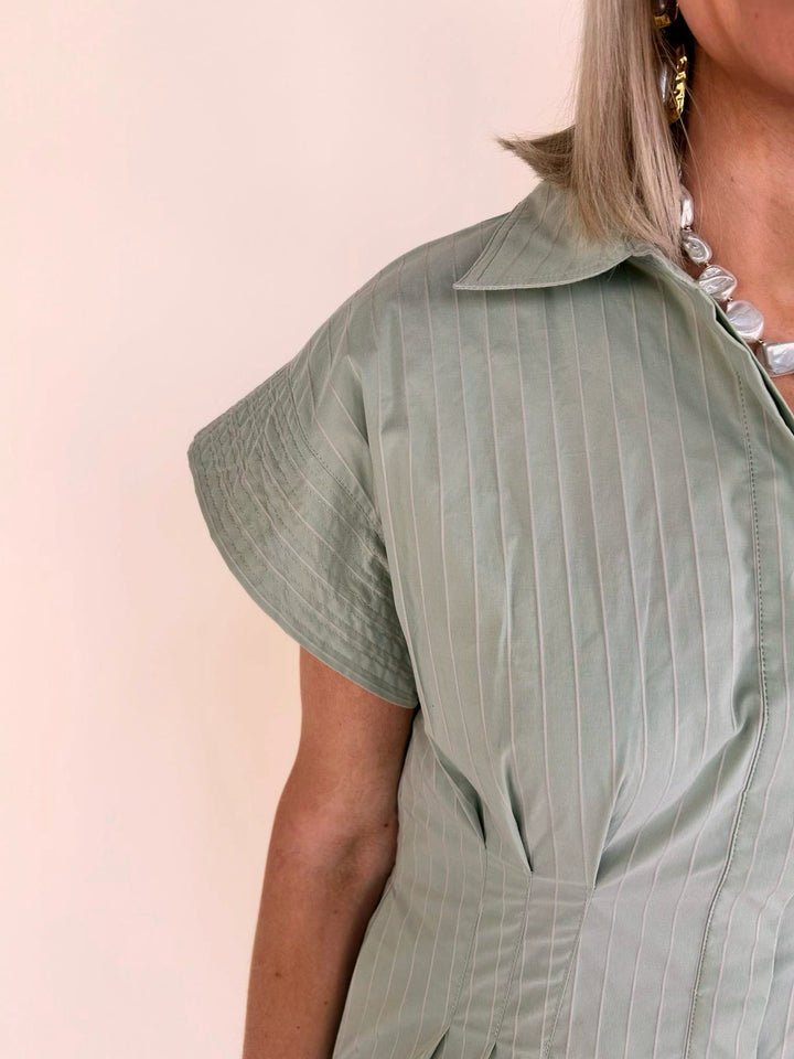 Close-up of the THML sage striped collared shirt dress featuring cap sleeves, pleated waist, and vertical stripe detail.