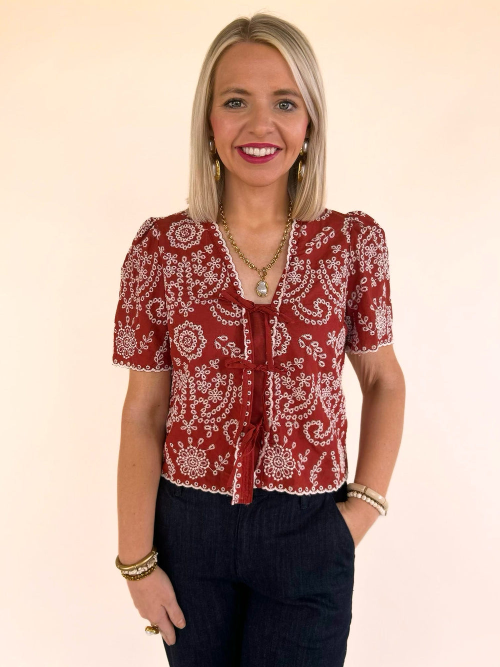 Women's burnt brick embroidered tie front blouse with V-neck, flutter sleeves, and dark denim jeans.