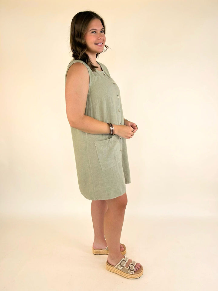 Angled front view of the Dear John Riri sleeveless linen blend dress in Abbey Stone with front pockets and relaxed silhouette.