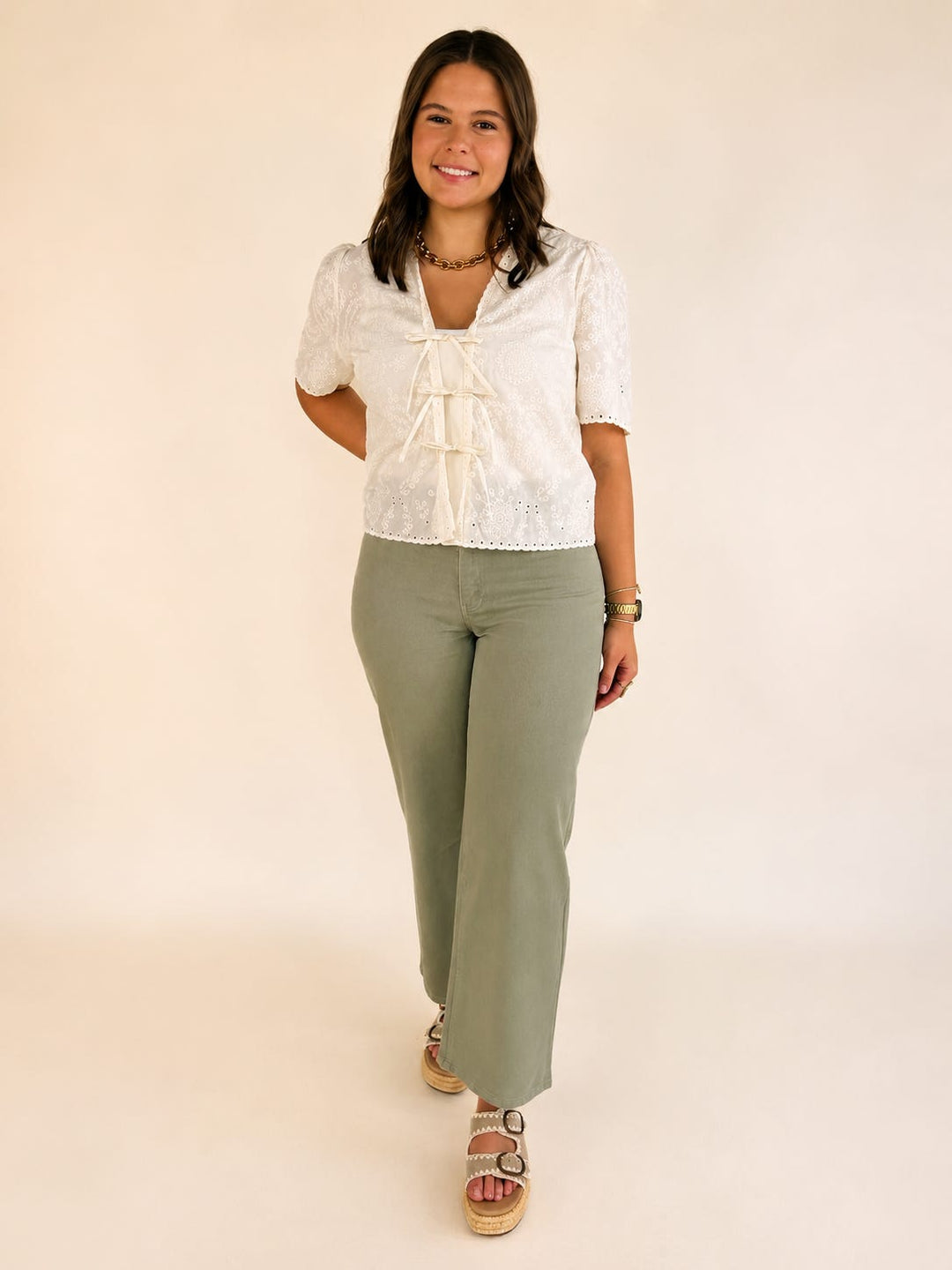 Women's cream embroidered tie front blouse with V-neck, flutter sleeves, and light olive wide leg pants.