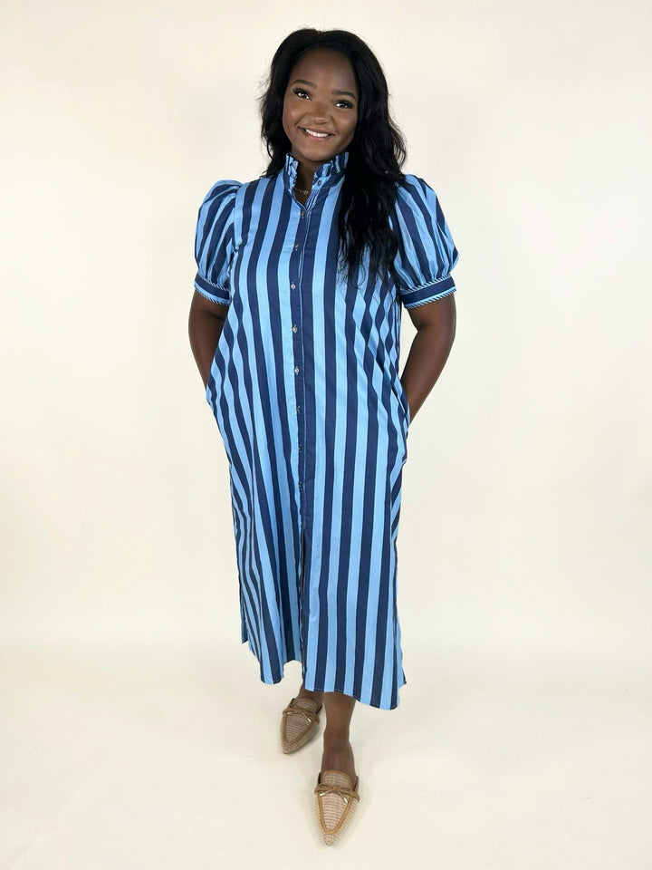 Model wearing a blue striped button-front midi dress with a ruffle mock neckline, puff sleeves, side pockets, and a relaxed silhouette styled with woven pointed-toe flats.