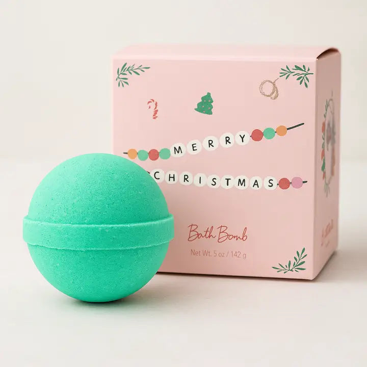 Green bath bomb in front of a pink 'Merry Christmas' box