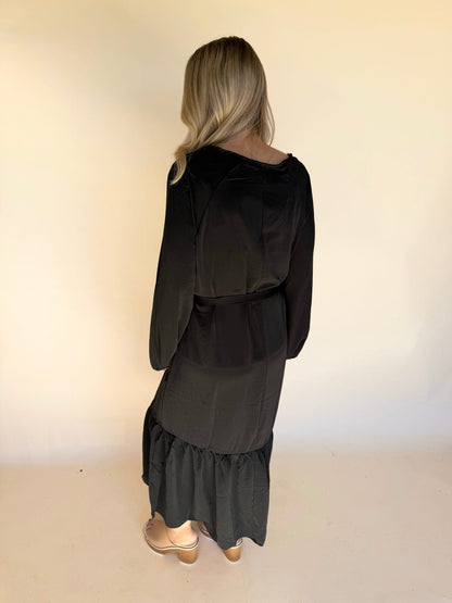 Person wearing a black dress with long sleeves and ruffled hem on a plain background