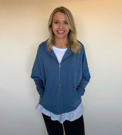 Woman wearing a blue zip-up hoodie over a white shirt against a plain background