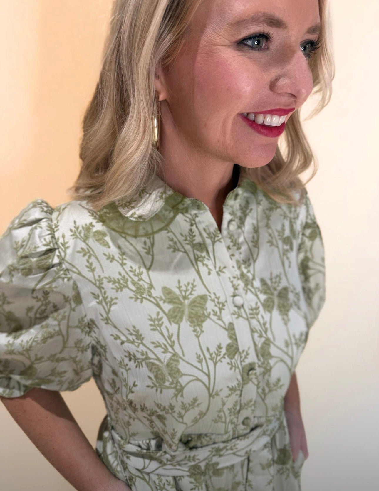 Close-up side view of light green floral print dress featuring puff sleeves, collared neckline, and fabric texture details, model smiling and wearing gold hoop earrings.