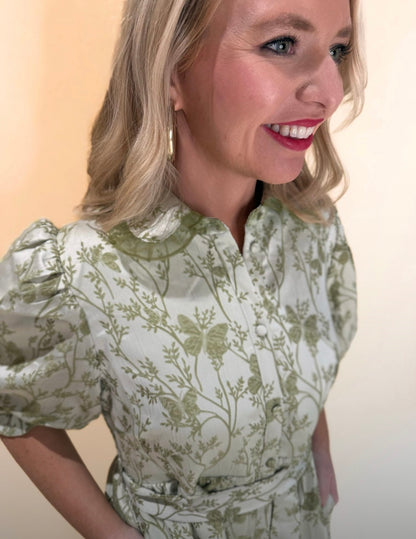 Close-up side view of light green floral print dress featuring puff sleeves, collared neckline, and fabric texture details, model smiling and wearing gold hoop earrings.