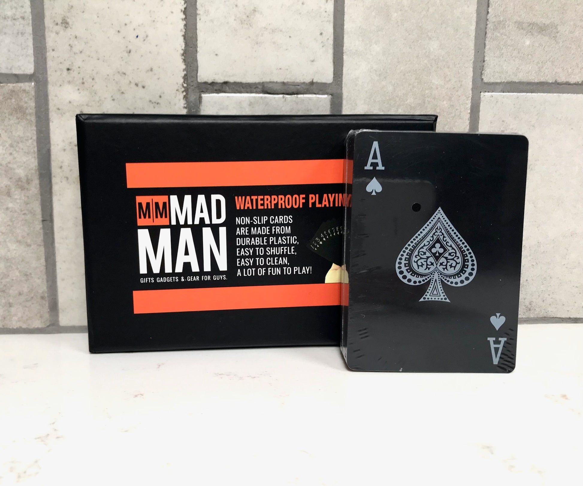 Black playing cards with Ace of Spades design and packaging labeled 'Mad Man' on a tiled floor background.