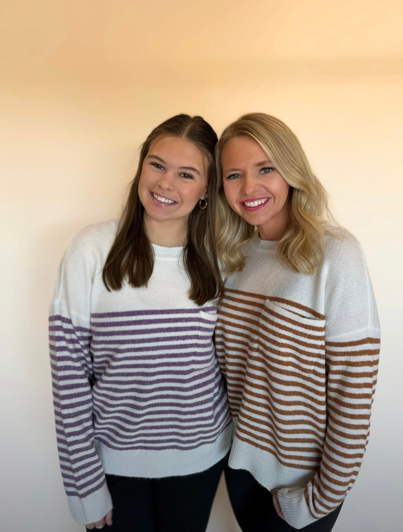 Two women wearing striped sweaters against a plain background