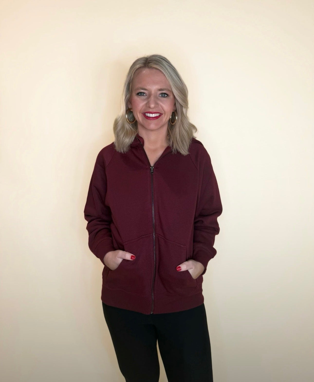 Back view of maroon zip-up hoodie showing hood and relaxed fit, paired with black leggings.