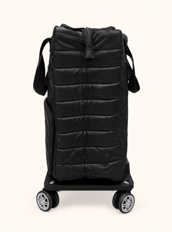 Side view of Simply Southern black quilted swivel rolling tote showing padded horizontal stitching, zippered closure, and spinner wheel base.