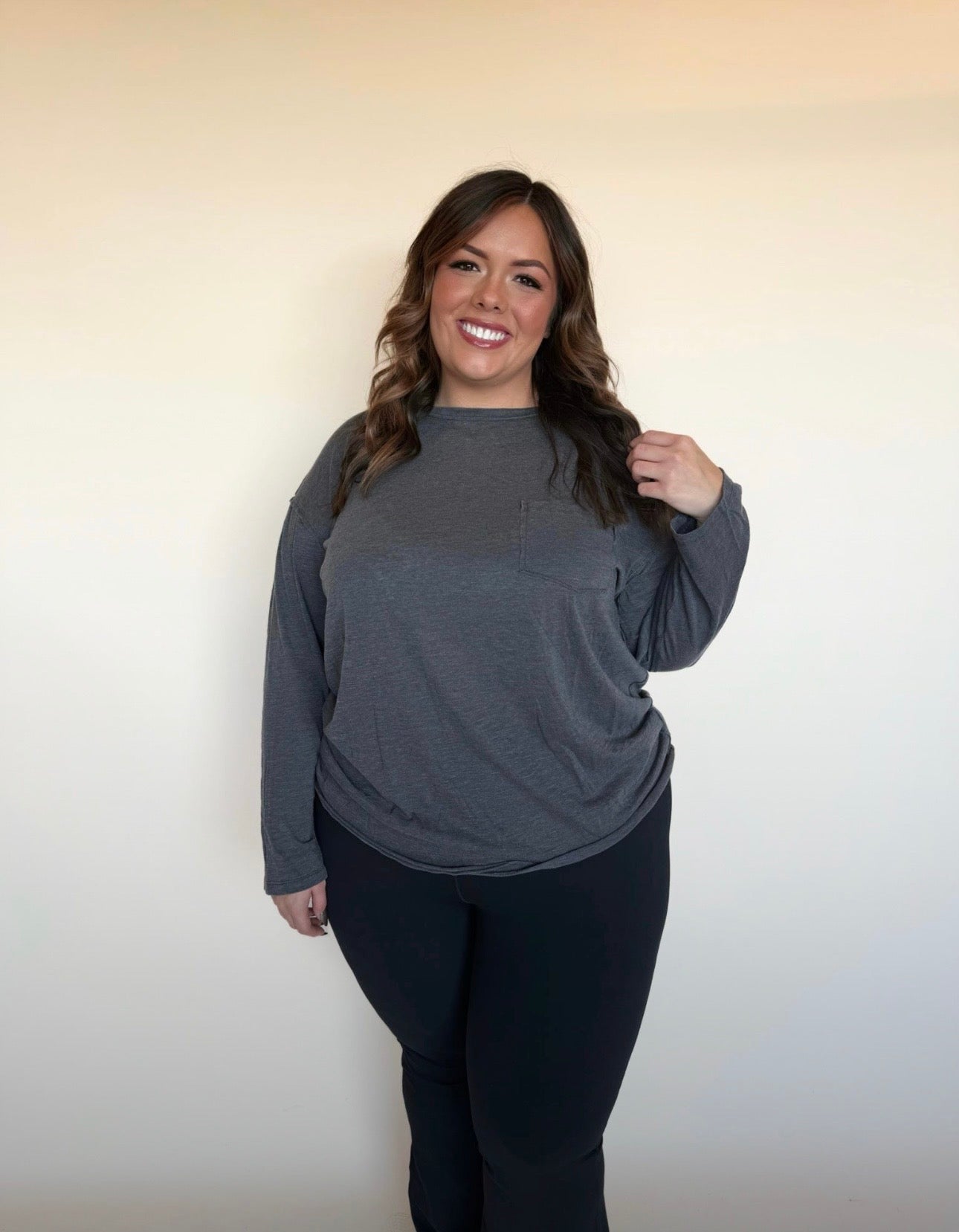 Woman wearing a gray long-sleeve top and black pants against a plain background