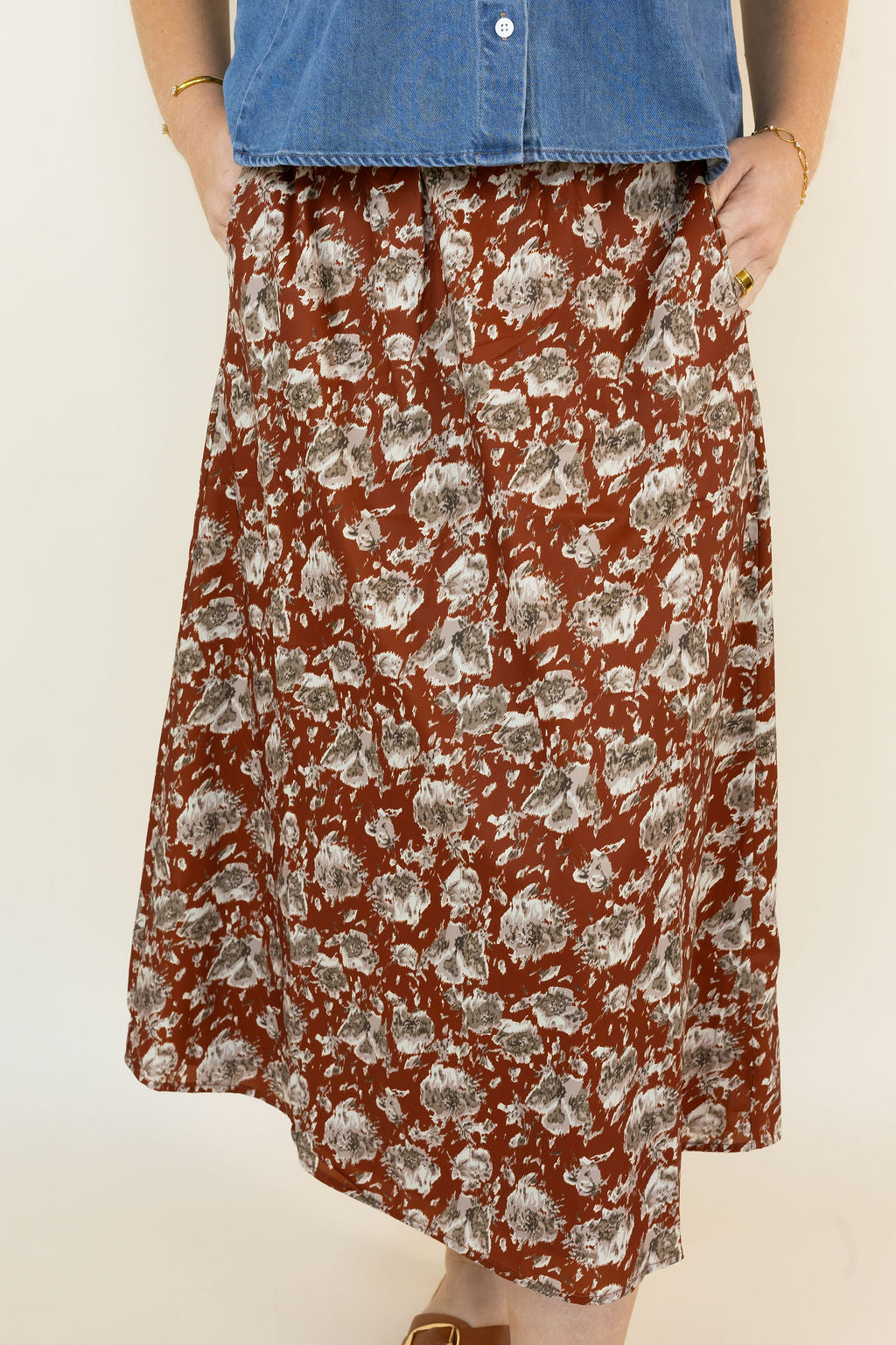 A person wearing a hickory midi skirt with a gray and white floral pattern, paired with a blue denim top, shown against a plain off-white background.