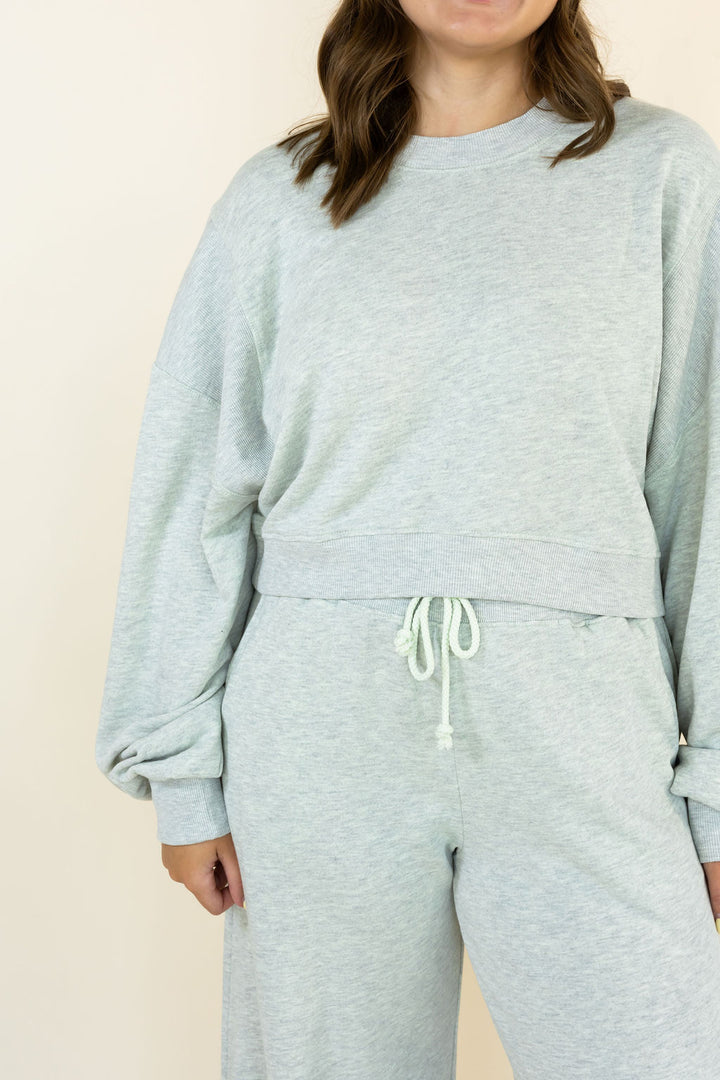 A person wearing a light heather gray sweatshirt and matching sweatpants with a white drawstring, shown against a plain cream background.