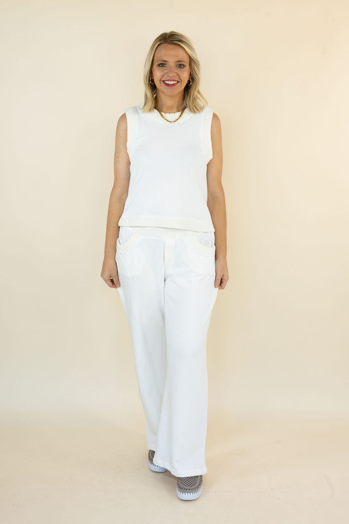 A woman modeling an ivory sleeveless top and matching ivory wide-leg pants against a plain beige studio backdrop.
