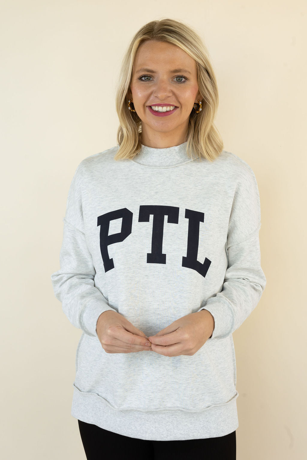 A smiling blonde woman wearing a light heather gray sweatshirt with &
