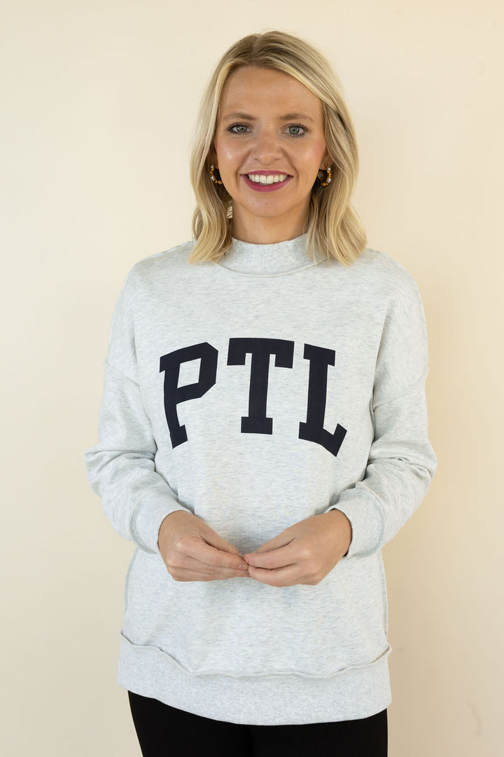 A smiling blonde woman wearing a light heather gray sweatshirt with &