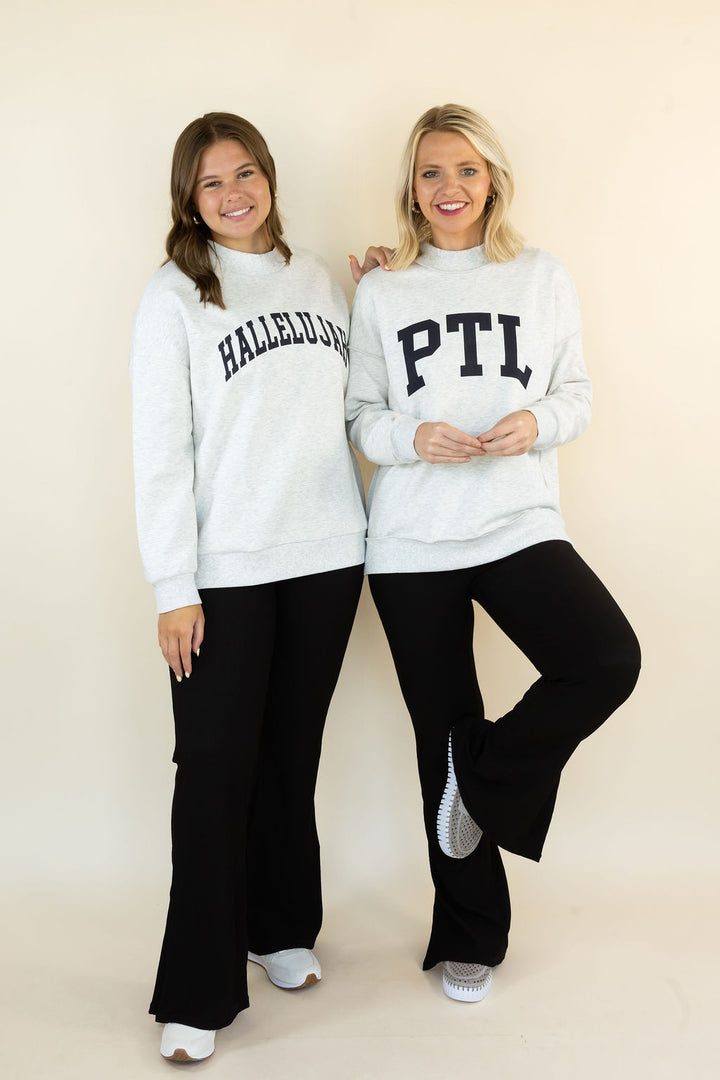 Two women modeling matching light gray sweatshirts with collegiate-style lettering, paired with black pants, standing against a plain beige studio background.