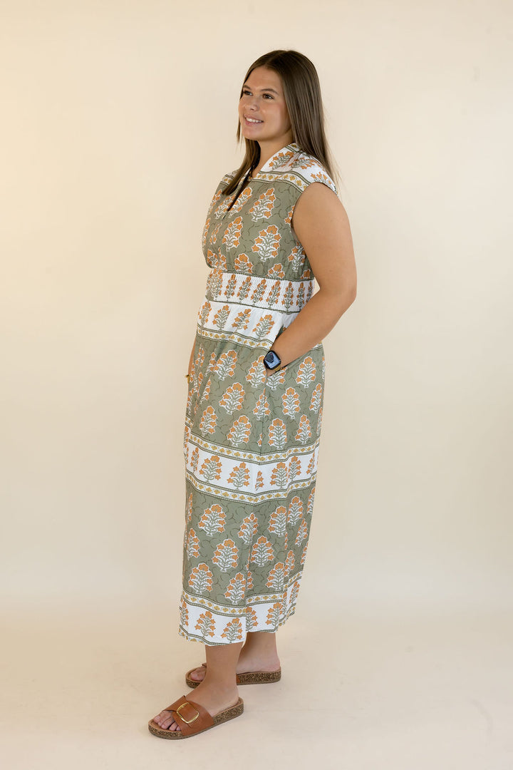 A woman modeling a sleeveless maxi dress with a green, white, and orange block print pattern, standing against a plain beige studio background.