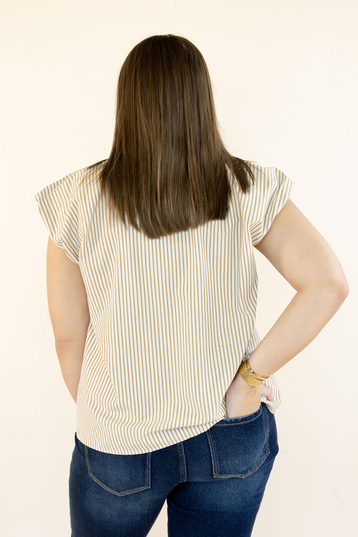 A woman viewed from behind wearing a cream-colored short-sleeve top with thin vertical yellow stripes and blue jeans, standing against a plain off-white background.