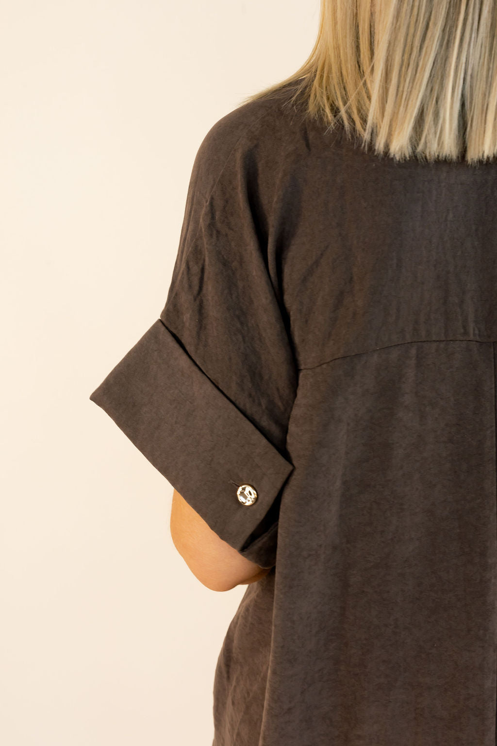 Close-up of chocolate brown maxi shirt dress showing wide cuffed short sleeves, button accent, and back seam detailing.