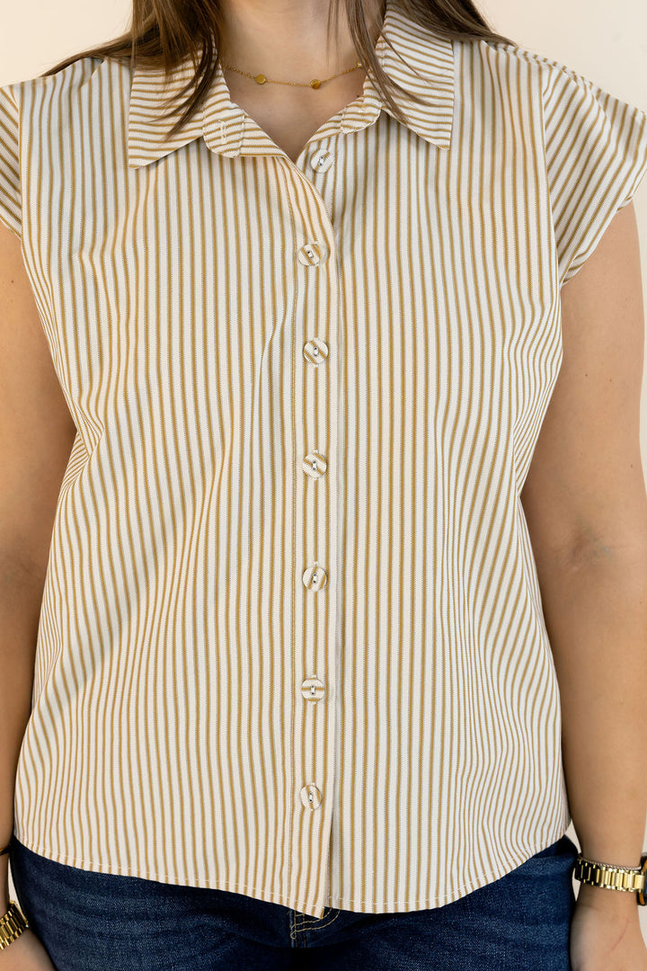 A woman wearing a sleeveless collared button-front top with vertical tan and cream stripes, paired with dark blue jeans.