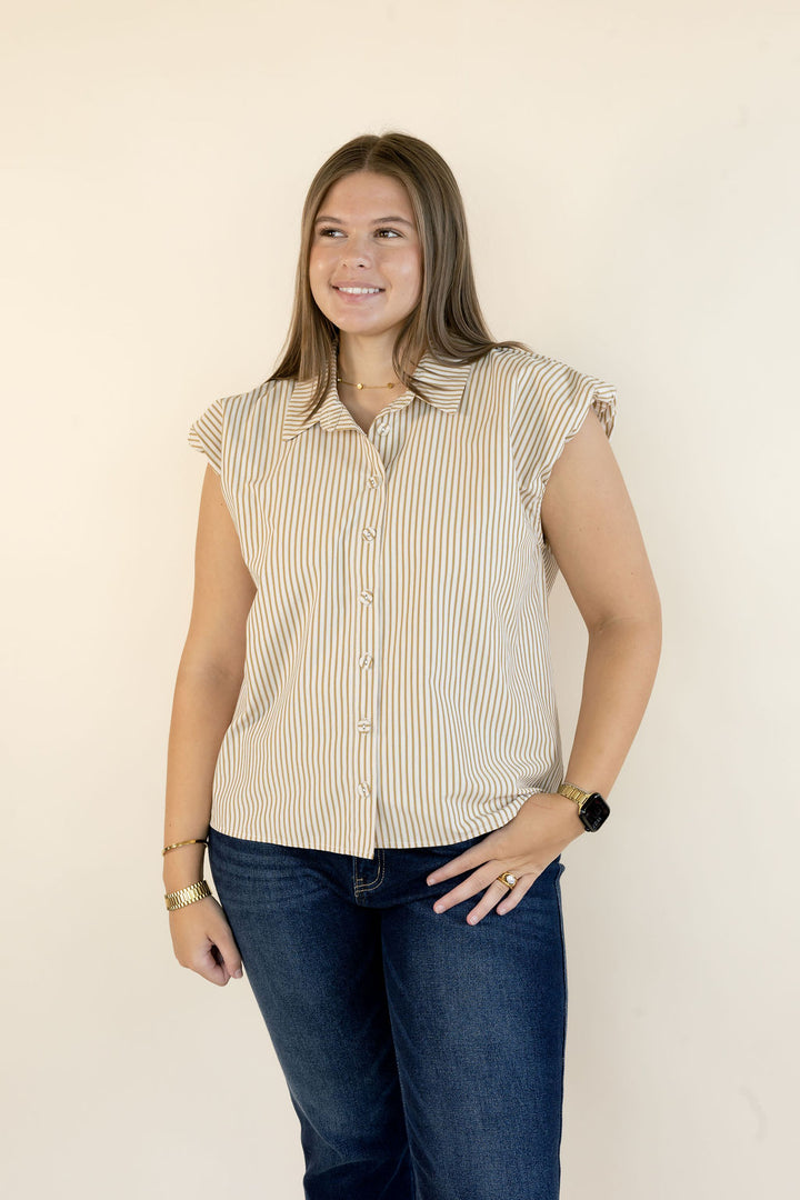 A woman modeling a sleeveless button-up shirt with vertical beige and white stripes, paired with dark blue jeans, standing against a plain off-white background.