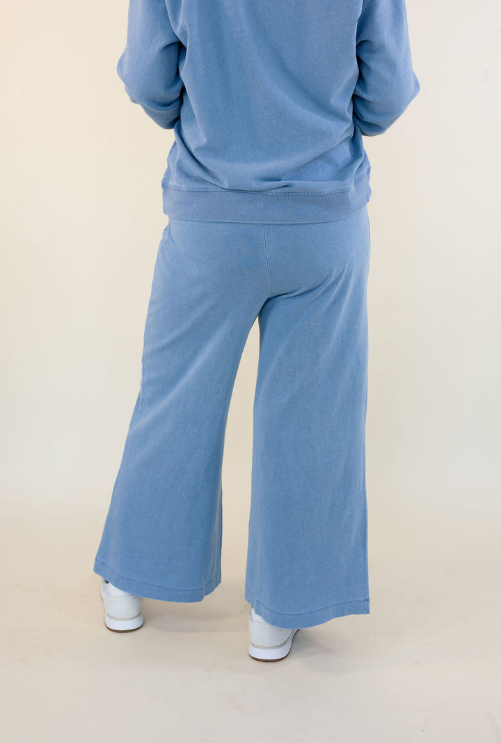 A person shown from the back wearing a light blue sweatshirt and matching wide-leg pants, standing against a plain light beige studio background.
