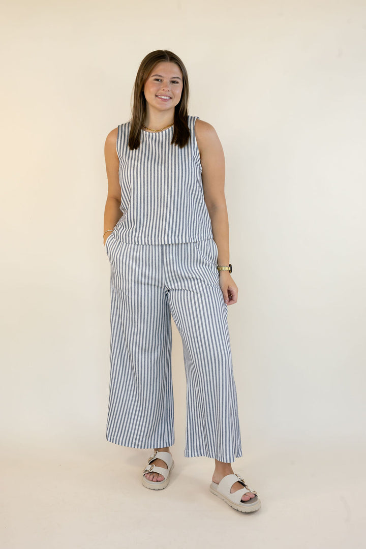 A woman modeling a sleeveless top and matching wide-leg pants set with vertical blue and white stripes, standing against a plain off-white studio background.