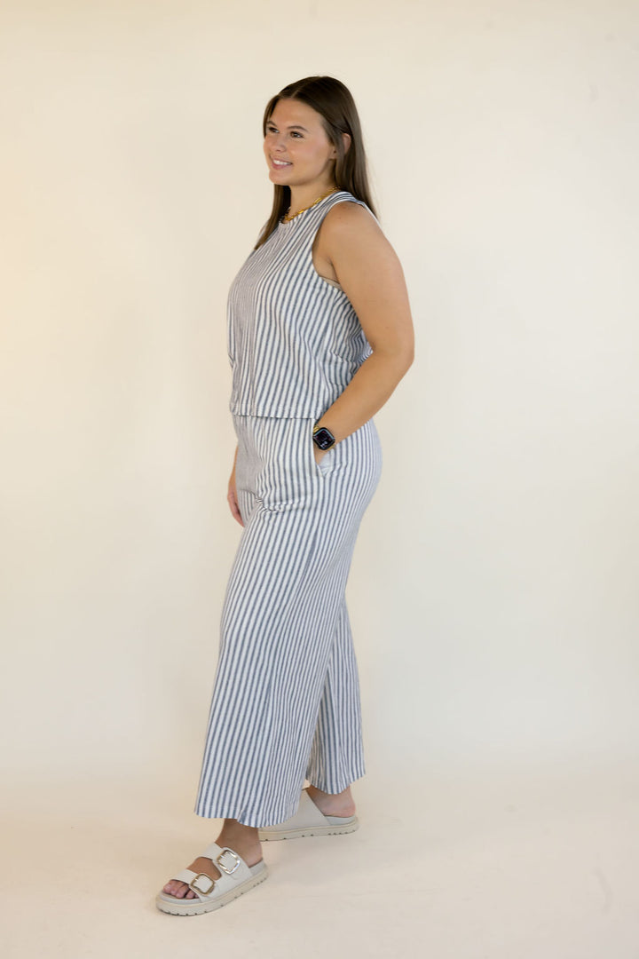 A woman modeling a sleeveless two-piece matching set with vertical blue and white stripes, standing against a plain off-white studio background.