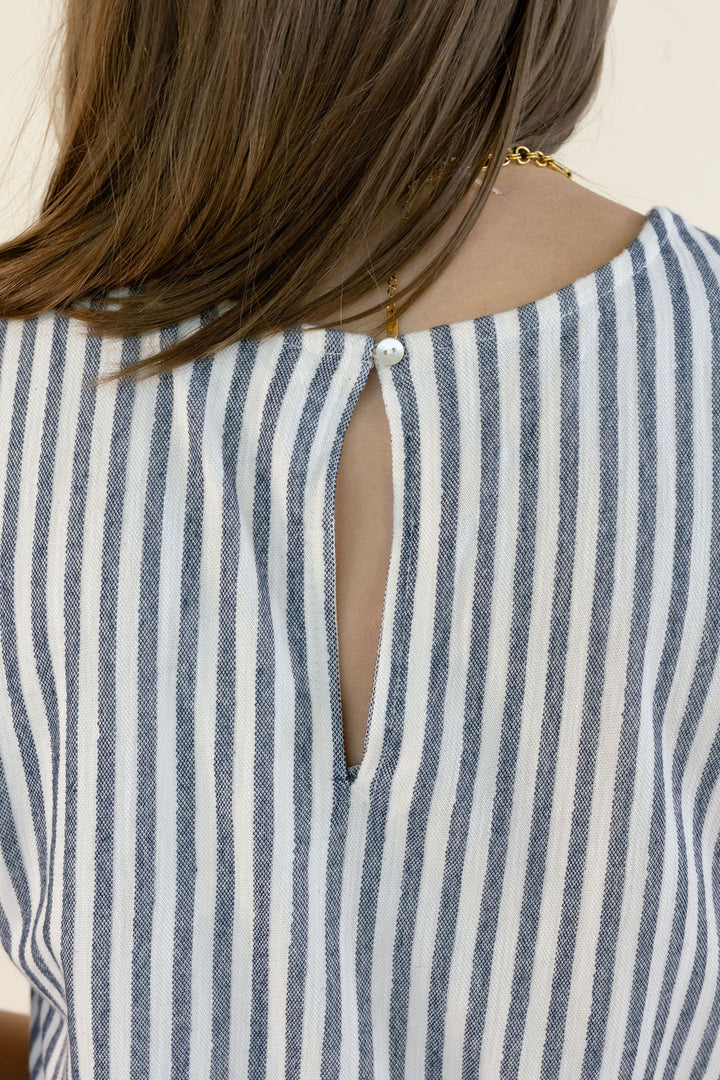 Close-up back view of a person wearing a blue and white vertically striped top, showing a keyhole back closure with a pearl-like center and a gold chain detail.