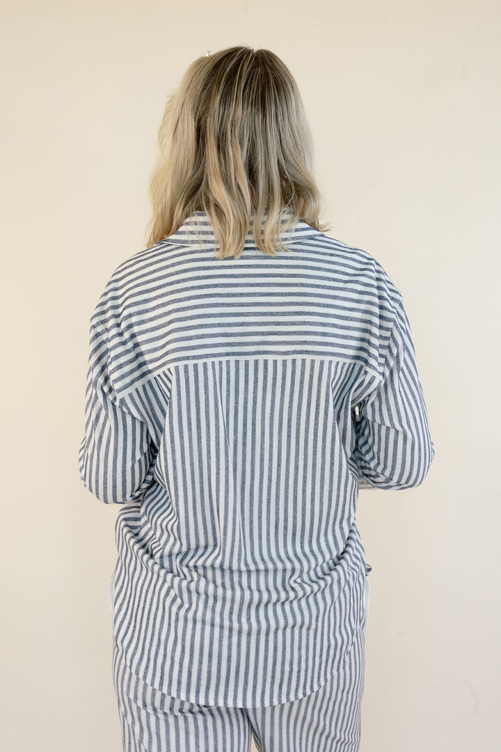 A person viewed from behind wearing a loose striped shirt and matching striped pants against a plain light beige wall.