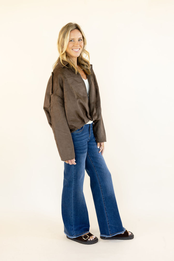 Side view of woman wearing dark brown faux suede cropped jacket with drop shoulders and cropped silhouette styled with blue jeans
