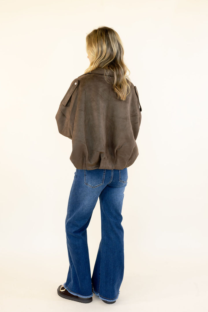 Full back view of woman wearing dark brown faux suede cropped jacket showing the relaxed boxy silhouette and ruched hem