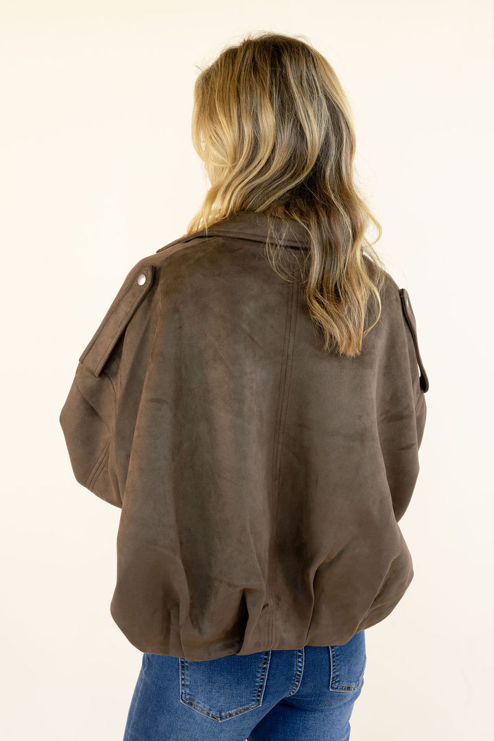 Close back view of dark brown faux suede cropped jacket highlighting the drop shoulders, epaulet details, long sleeves, and gathered ruched hem