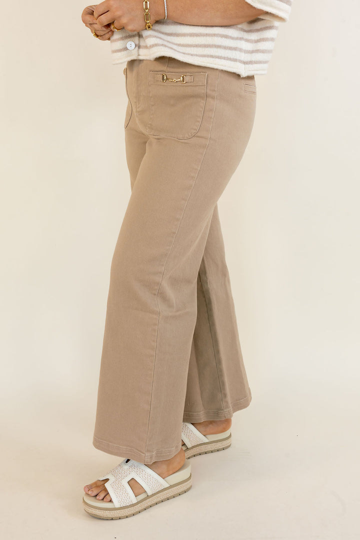 Side view of woman wearing taupe cropped wide leg pants with front patch pockets, gold zipper detail, and casual sandals