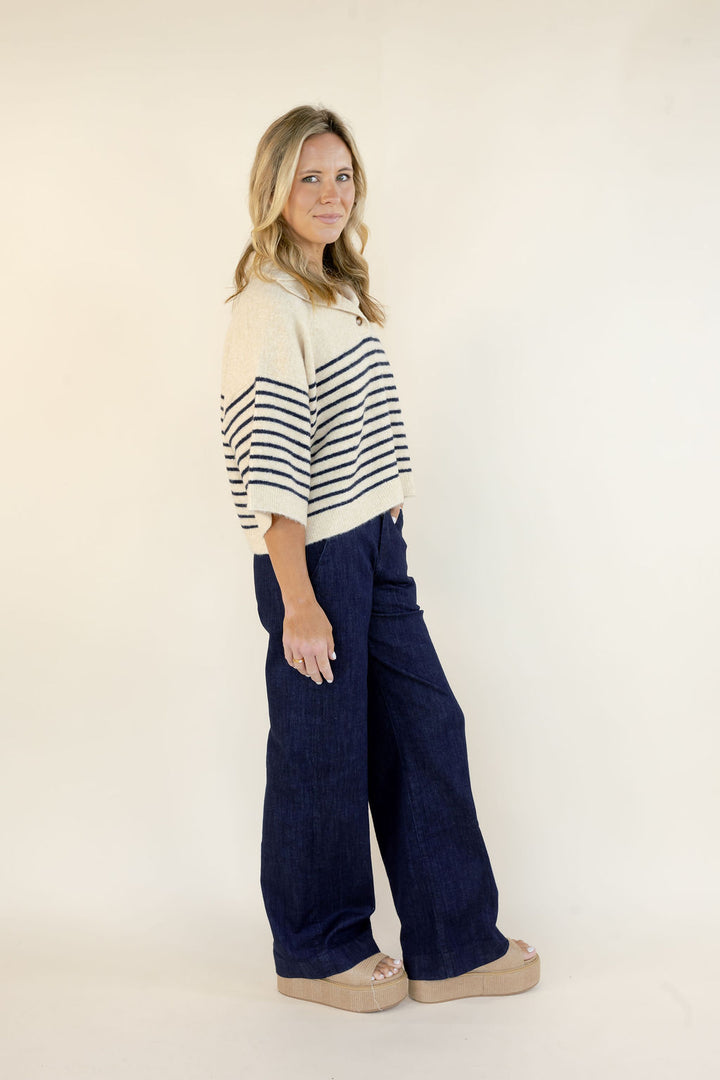 A woman modeling a cropped knit sweater with cream and navy horizontal stripes and wide-leg navy pants, standing against a plain off-white studio background.