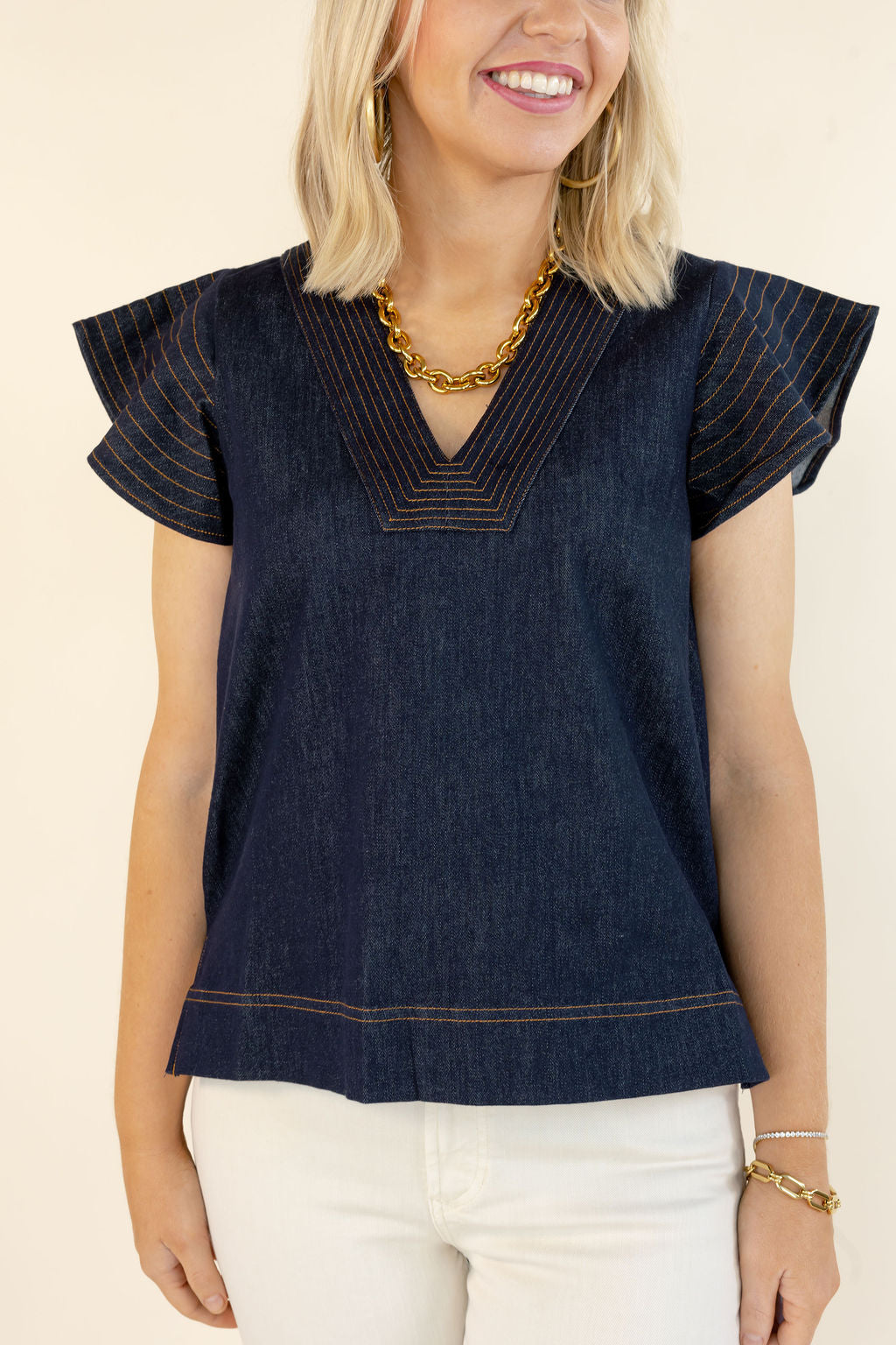 Closer front view of THML denim blue V-neck top showing layered flutter sleeves, contrast stitching, and relaxed silhouette
