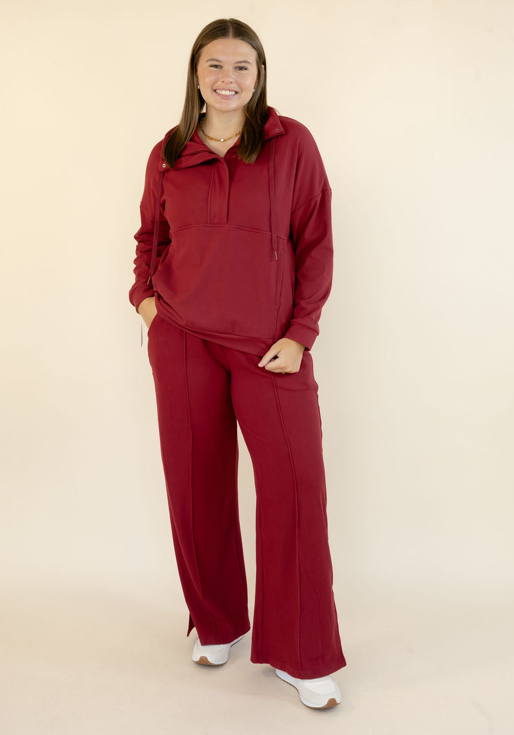 Woman modeling deep red matching lounge set with hooded pullover and relaxed wide leg pants styled with white sneakers