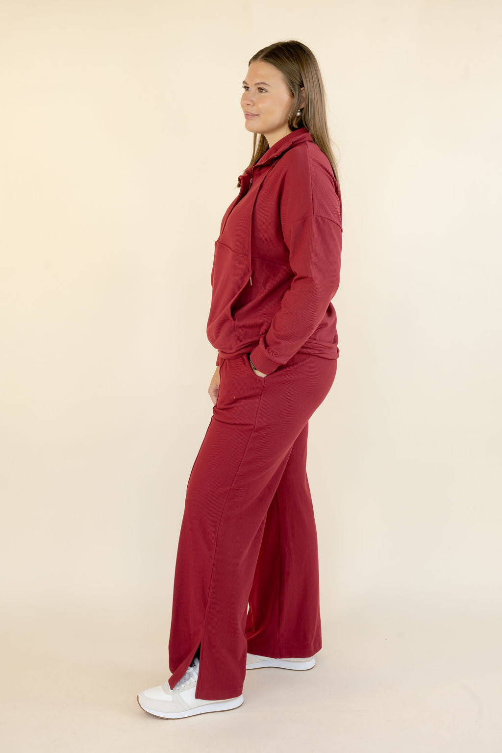 Side view of woman wearing deep red matching lounge set with hooded pullover and wide leg pants
