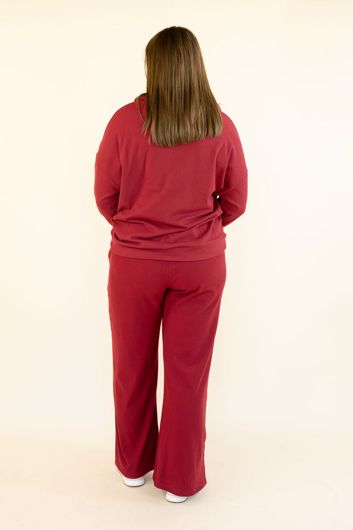 Full back view of woman wearing deep red hooded pullover and matching wide leg pants with relaxed fit