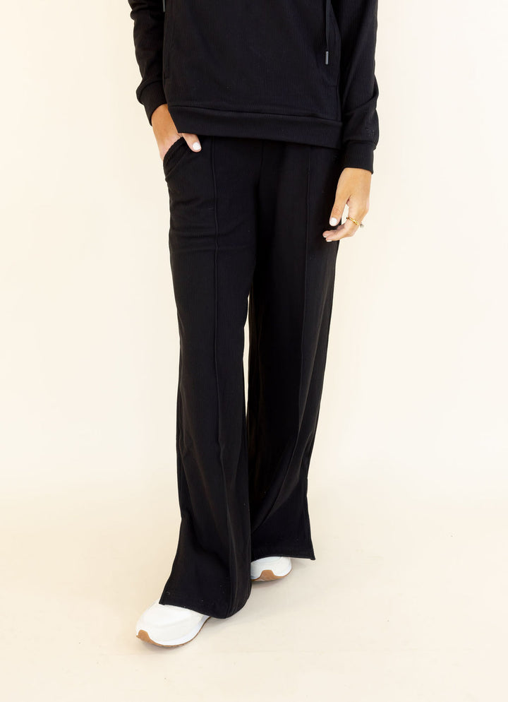 Front view of black wide leg pants featuring a relaxed full-length silhouette and side pockets