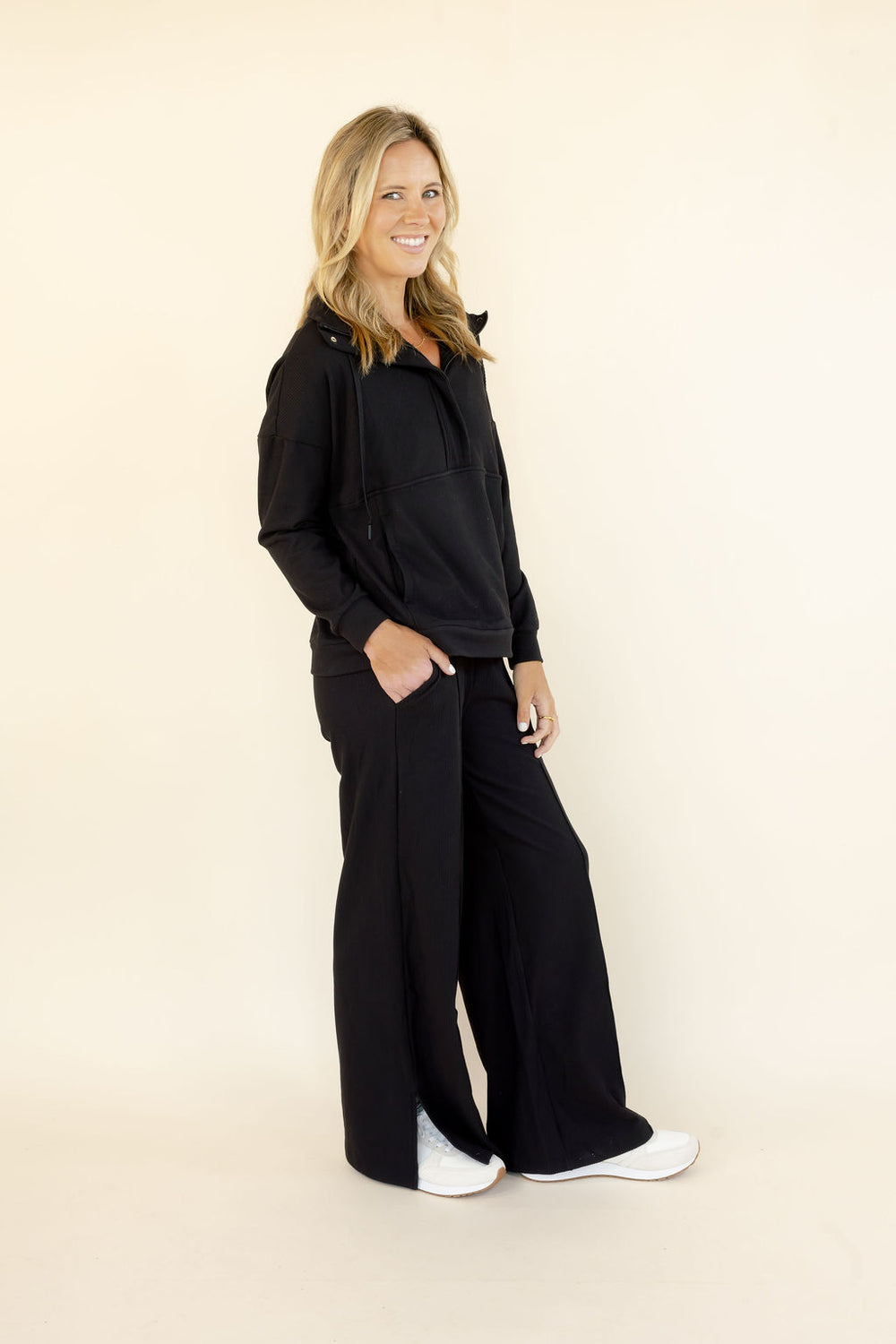 Three-quarter view of woman wearing black half-zip hooded pullover and matching wide leg pants with relaxed fit