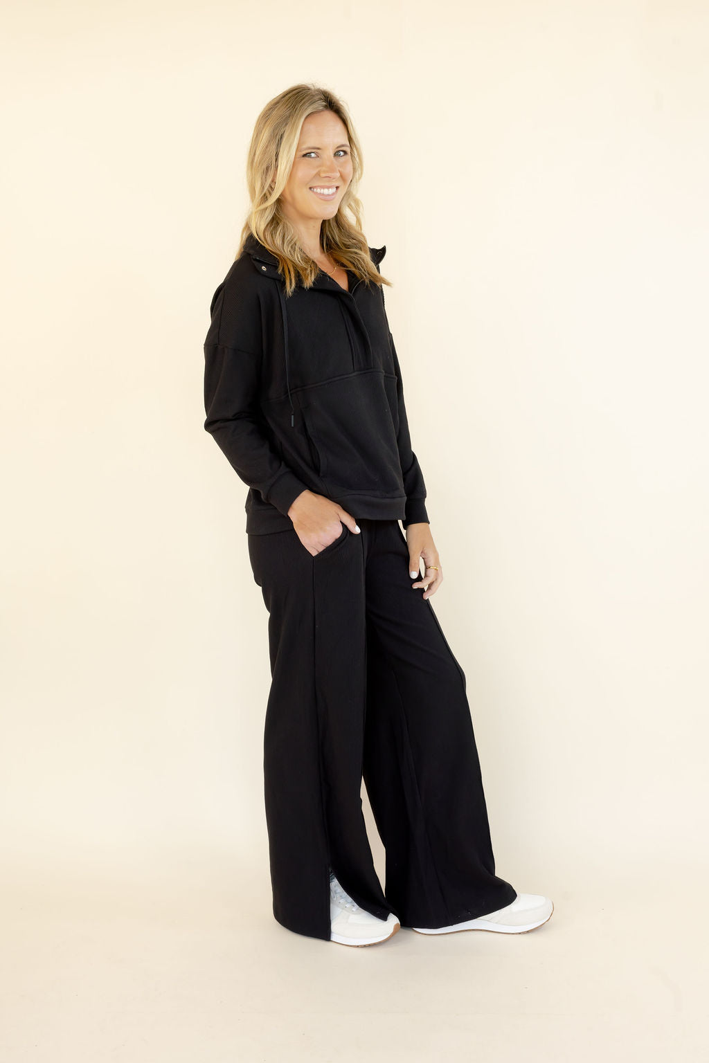 Three-quarter view of woman wearing black half-zip hooded pullover and matching wide leg pants with relaxed fit
