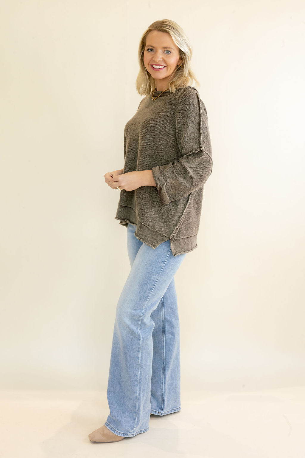 A woman modeling a washed brown 3/4 sleeve top and light blue flare jeans against a plain cream studio background.