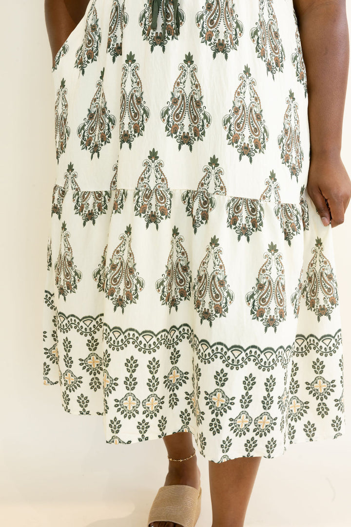 Close-up of ivory and olive green botanical print midi dress showing the tiered skirt and coordinating decorative border print at the hem
