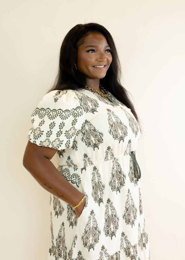 Side view of ivory botanical print midi dress featuring olive green pattern, puff sleeves, side pockets, and flowy tiered silhouette