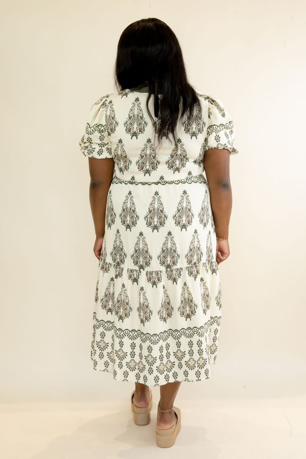 Back view of ivory and olive green botanical print midi dress showing puff sleeves, relaxed fit, tiered skirt, and printed border hem